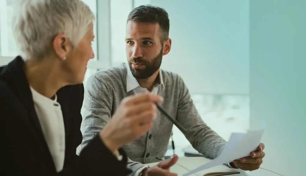Twee personen in gesprek aan tafel, met een document in de hand