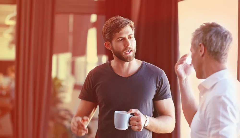 Twee mannen in gesprek, een van hen houdt een mok vast