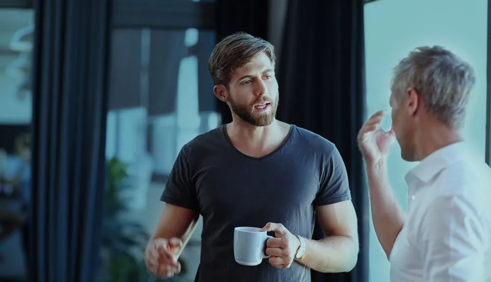 Twee teamleden in een open gesprek met een kop koffie